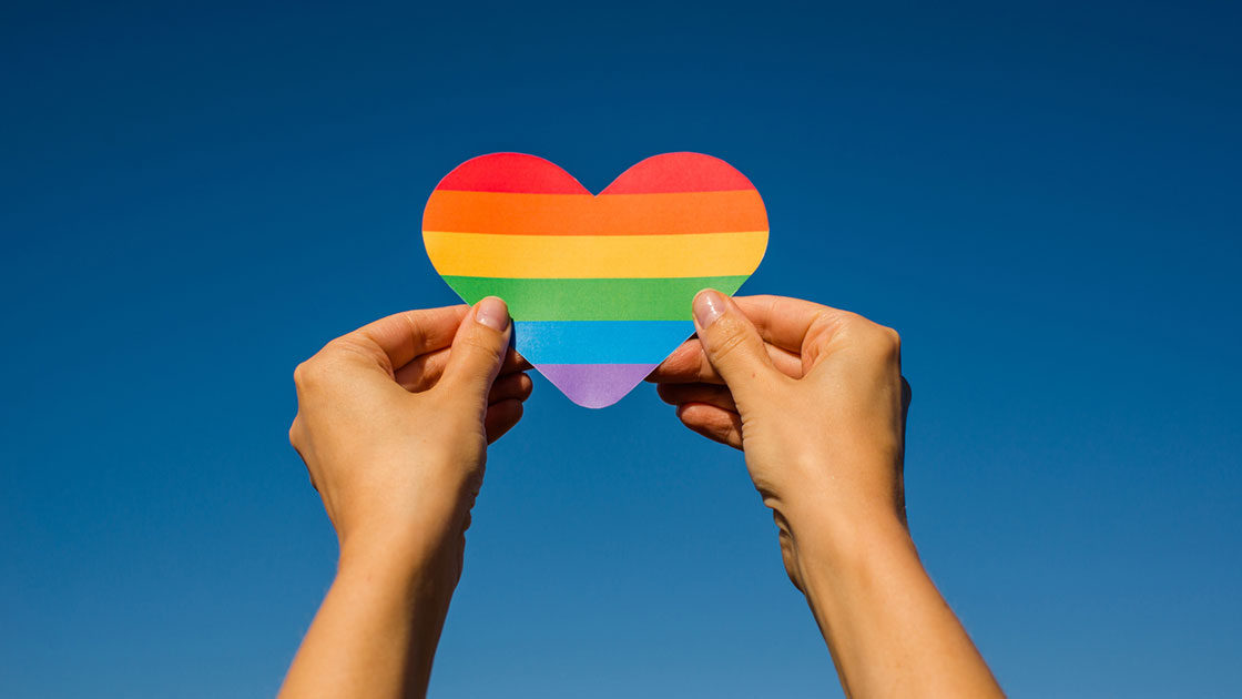 Hands holding up a rainbow lgbtq heart